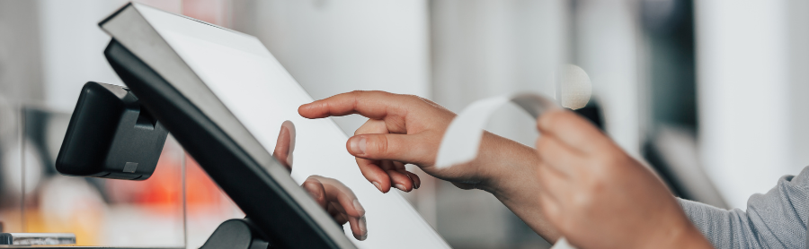 a man's hand touching the POS system while holding a receipt