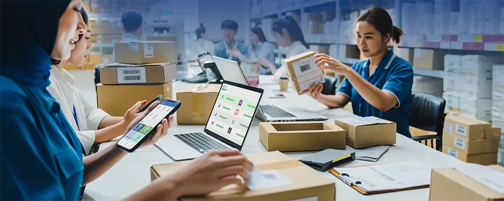 Warehouse team packing and labeling parcels while a staff member uses the SiteGiant ONE mobile app to cross check items.